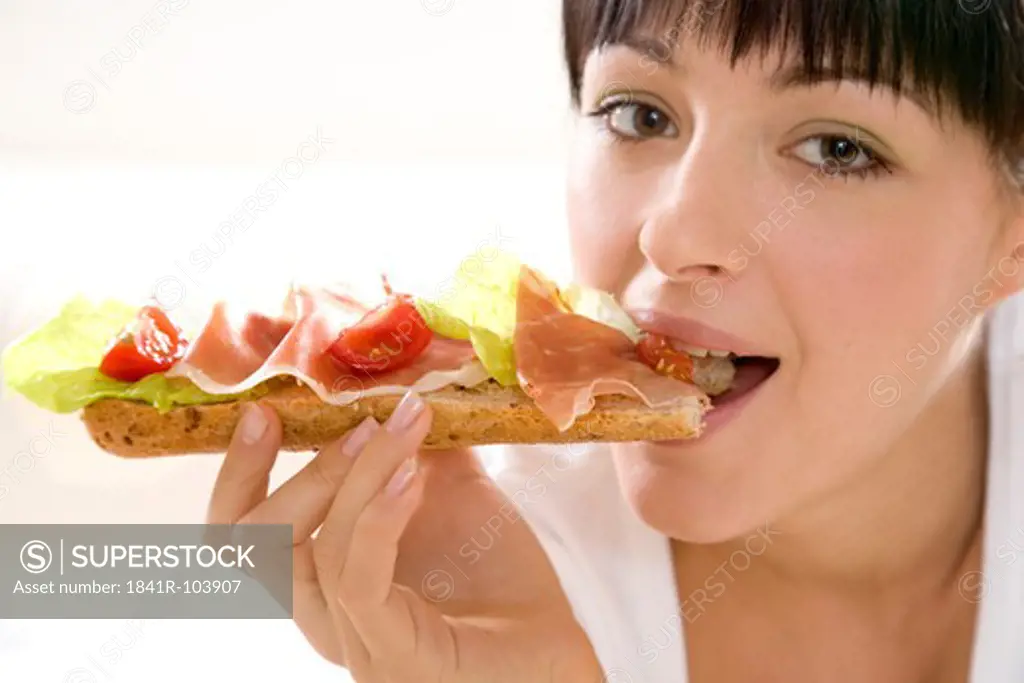 woman eating sandwich with ham and tomato