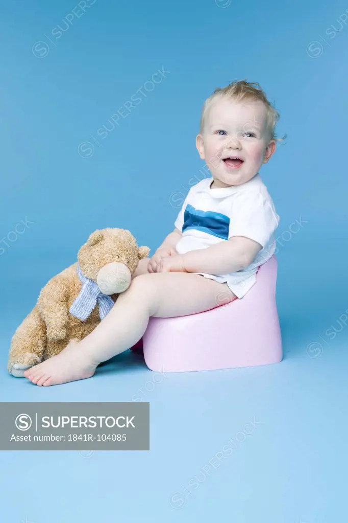 small boy sitting with teddy bear on toilet