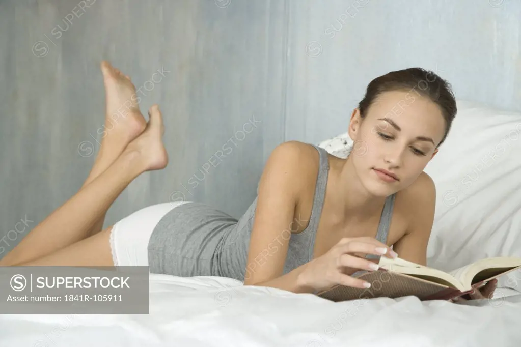 young woman reading book in bed