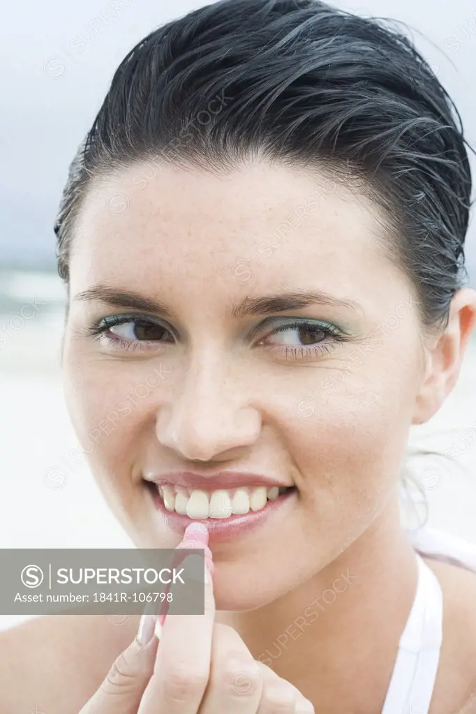 woman putting lipbalm on beach