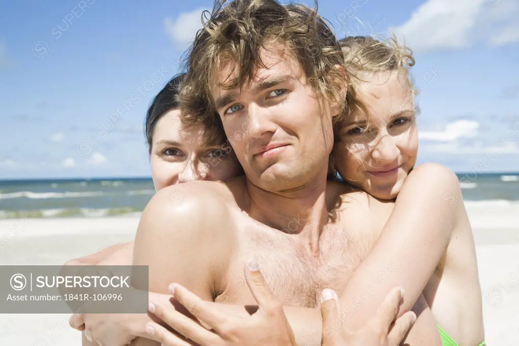 two girls hugging boy on beach
