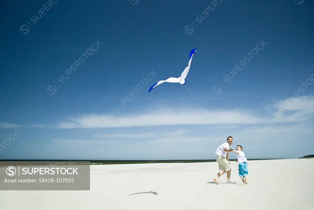 father and son playing with kite on beach