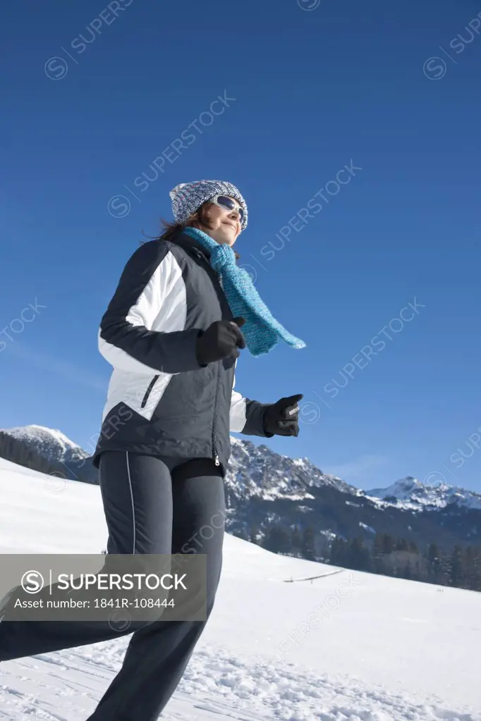 Smiling woman jogging in winter landscape, Tannheimer Tal, Tyrol, Austria