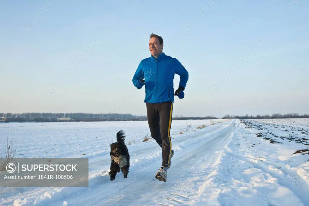 Man jogging in snow with dog, Tannheimer Tal, Tyrol, Austria