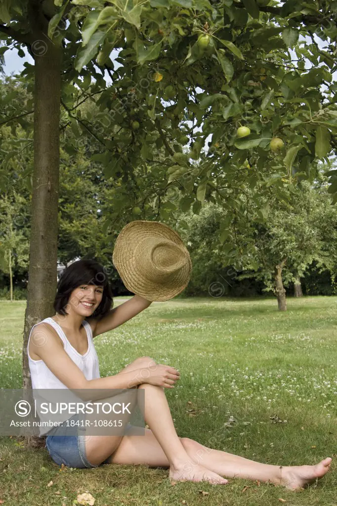 Happy young woman sitting at apple tree