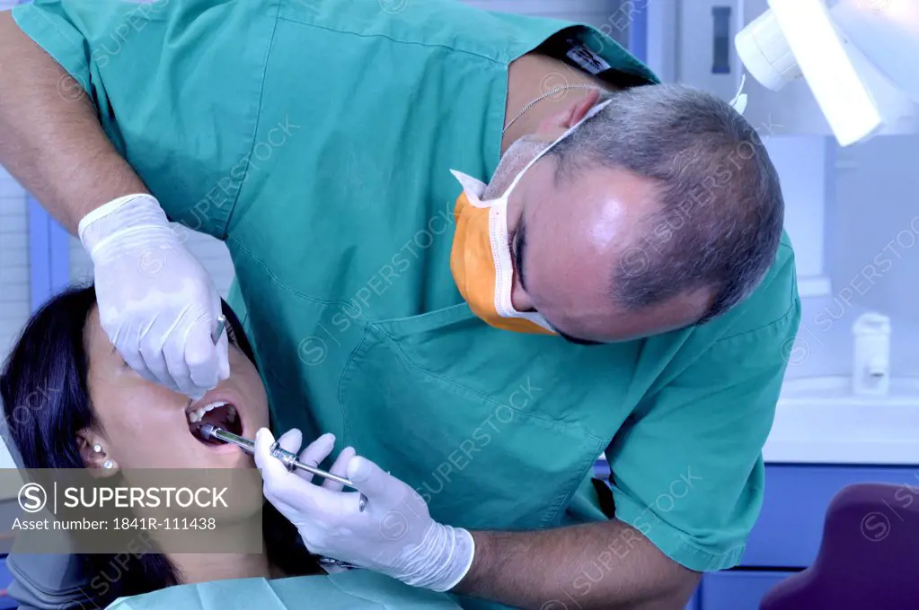 female patient at the dentist sitting at the surgery couch  - dentist's assistant in the back