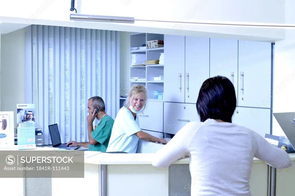 female patient and female medical assistant at the reception - male doctor at the background