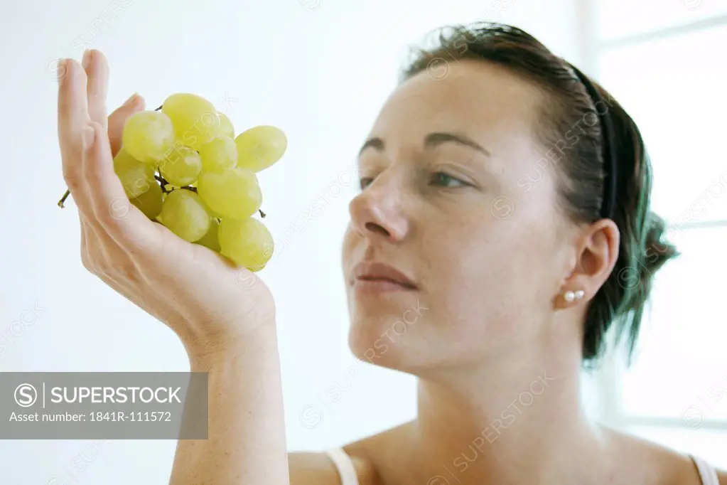 Young woman is looking at a bunch of grapes.