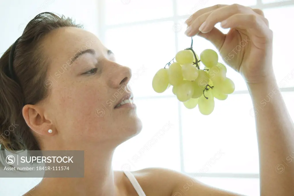 Young woman is looking at a bunch of grapes.