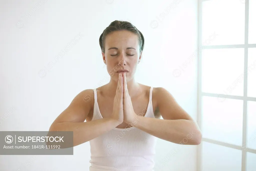 Young woman folds her hands meditatively in front of her chest.