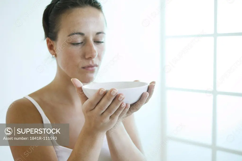 Young woman holding a bowl in front of her face.