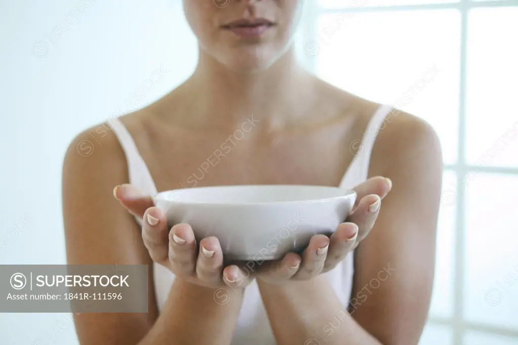 Young woman holding a bowl in front of her chest.