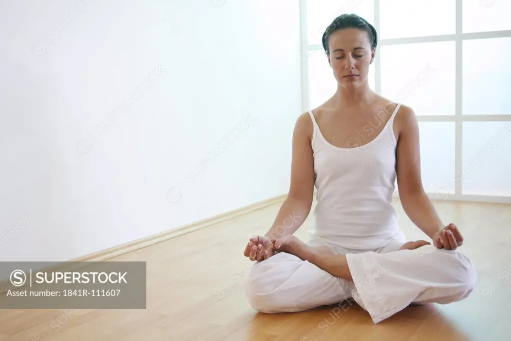 Young woman meditates in lotus position on the floor.