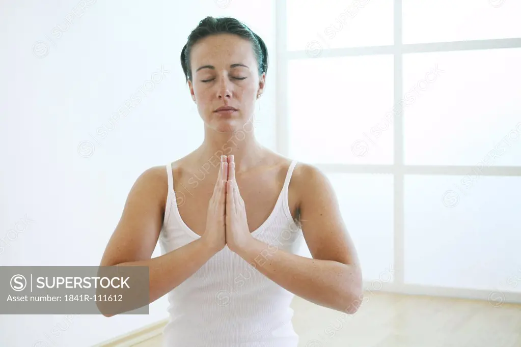 Young woman folds her hands meditatively in front of her chest.