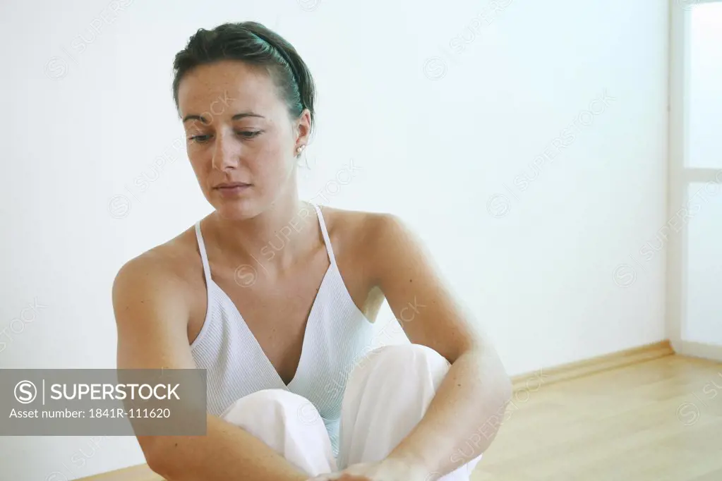 Young woman sits with tucked up legs on the floor.