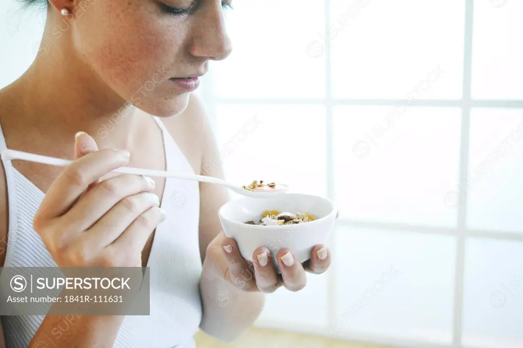 Young woman holds a bowl of cereals and a spoon.