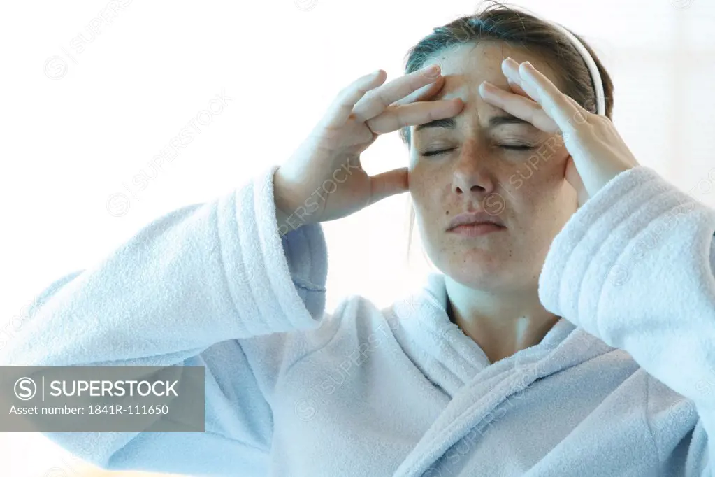 young woman having headache dressed in a white bath robe holding her hands at the forehead