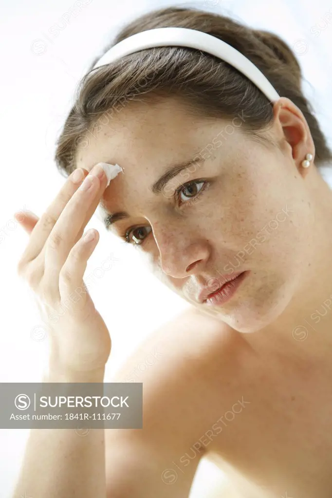 portrait of a young woman using face cream at her forehead - facial care product