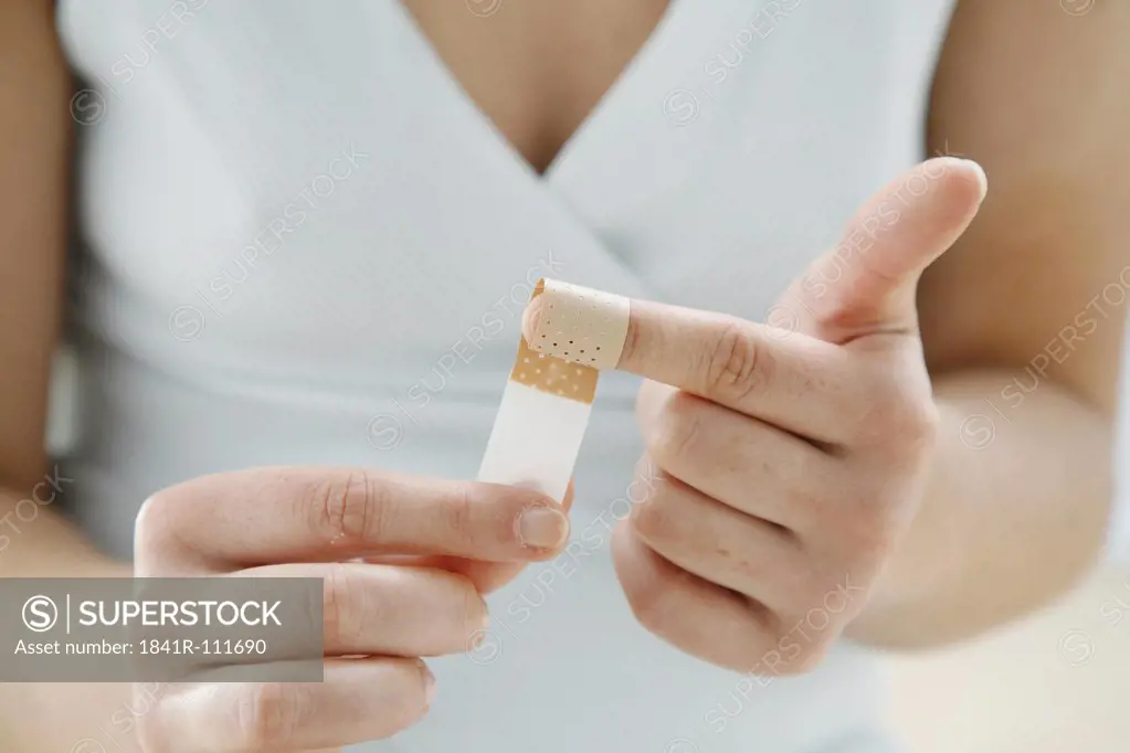 close up - young woman is  wraping  a plaster around her index finger- band-aid