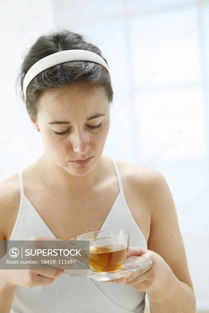 young woman looking sad is holding a cup of tea in her hands