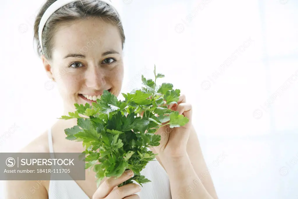young woman holding a bunch of lovage in her hands and is taking a smell on it