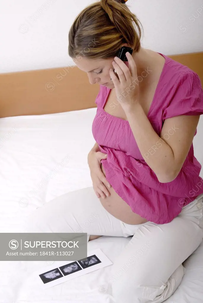Pregnant woman with mobile phone looking at ultrasound pictures