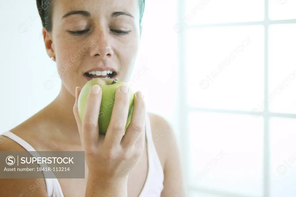 Young woman eating a green apple.