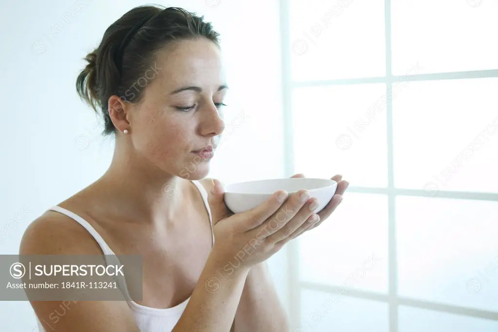 Young woman holding a bowl in front of her face.