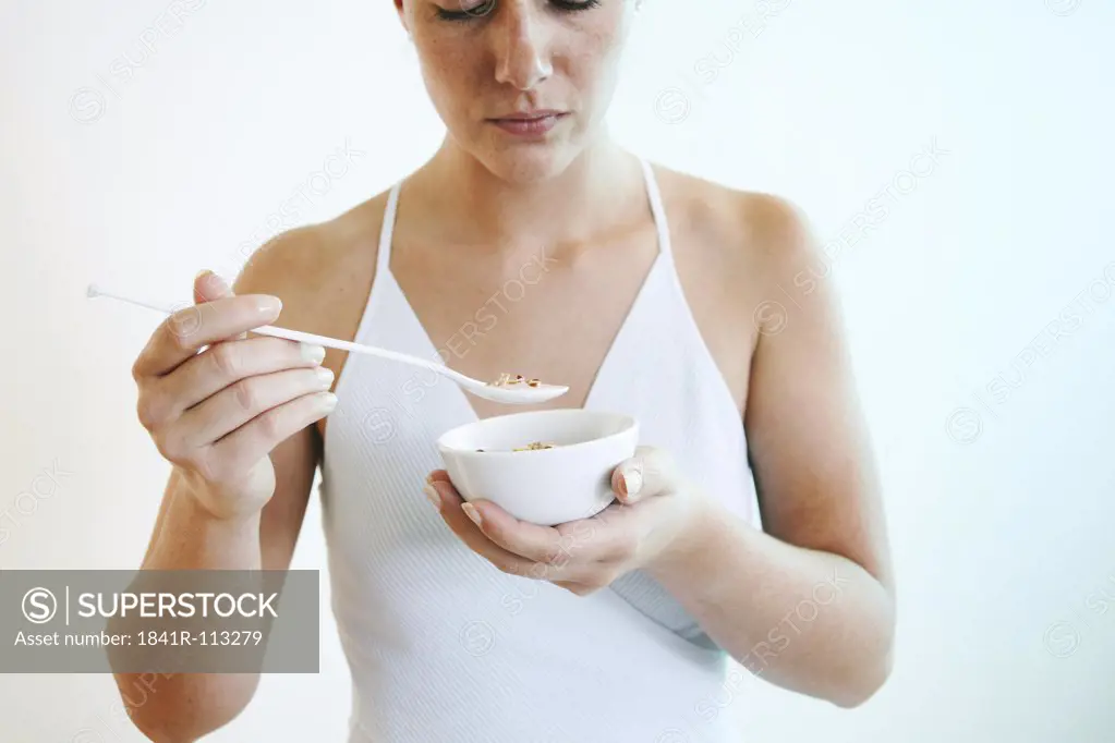 Young woman holds a bowl of cereals and a spoon.
