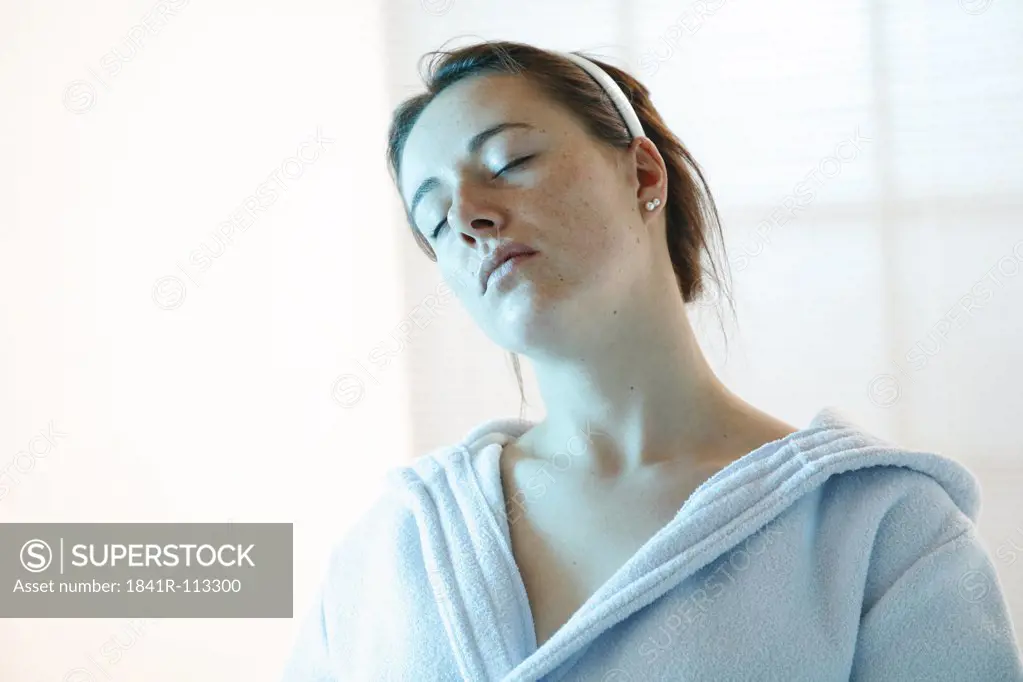young woman with closed eyes dressed in a white bath robe holding her head sidewards fŸr recreation