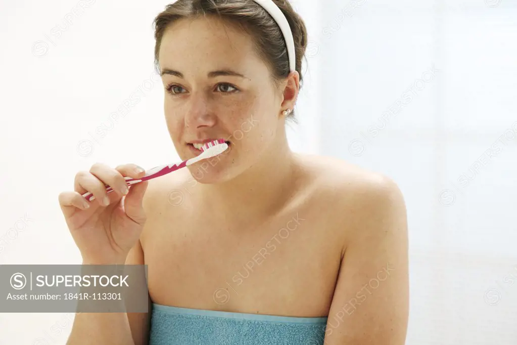 young woman dressed with a towel is cleaning her teeth with a toothbrush