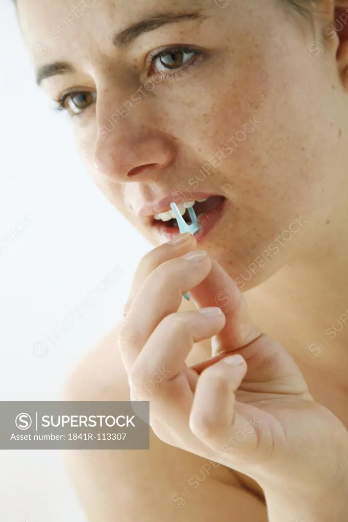 portrait of a young woman cleaning her teeth with dental floss