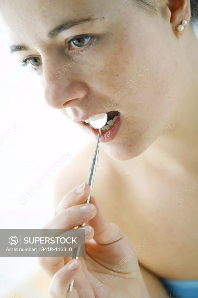 young woman checking out her teeth with a stomatoscope
