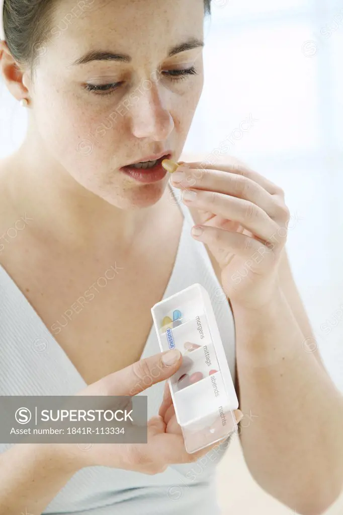 young woman holding a pill box in her hand and taking on of the tablets into her mouth
