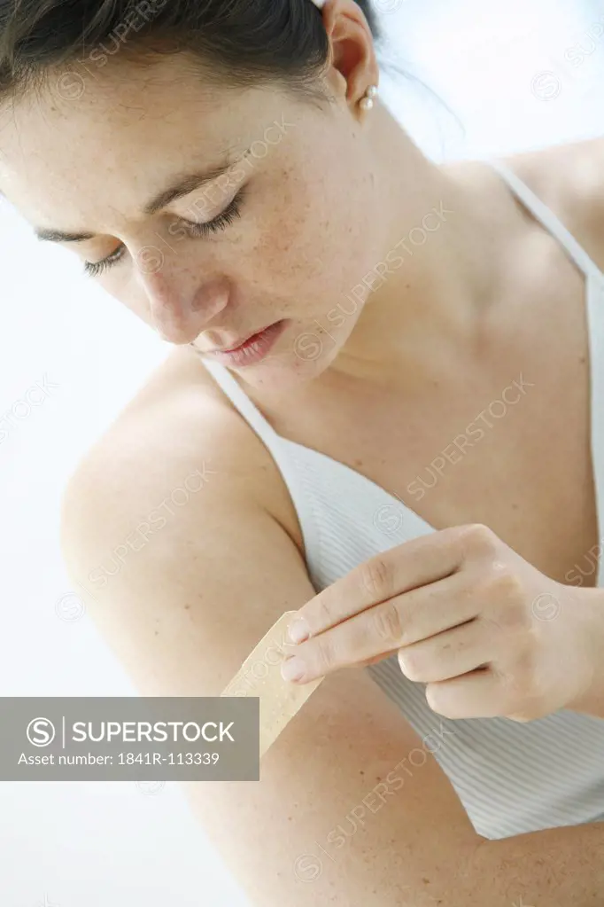 young woman is sticking a plaster on her upper arm -band-aid
