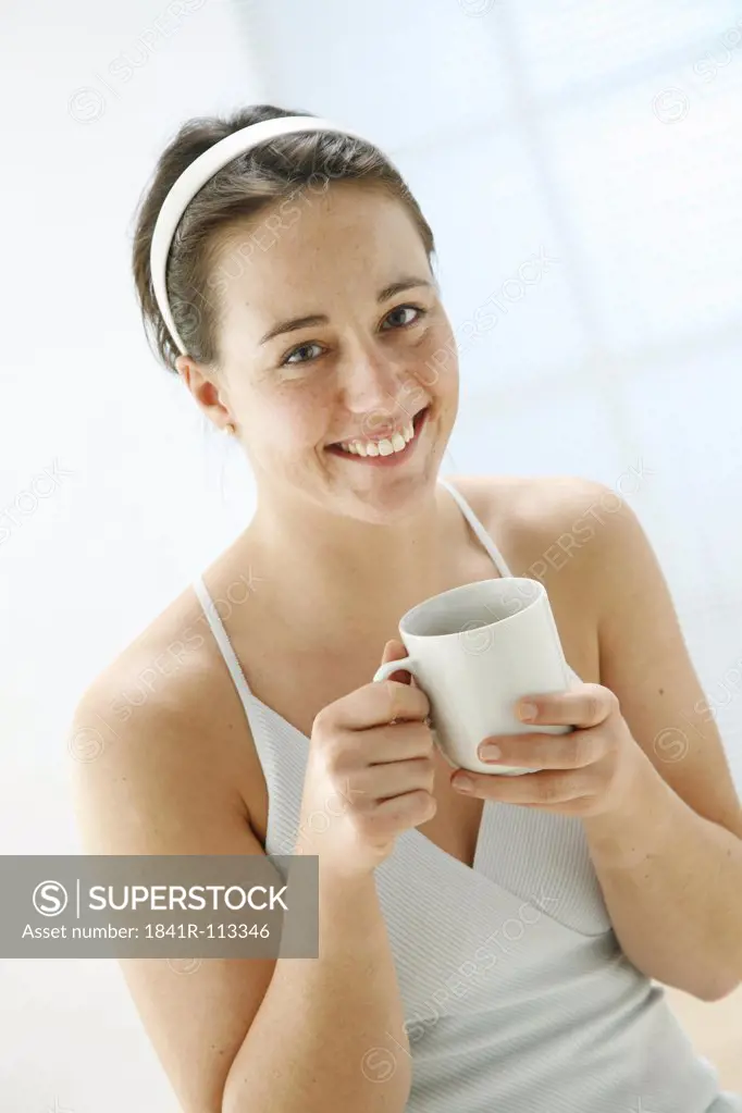 young woman holding a cup of tea in her hands and is smiling at the camera
