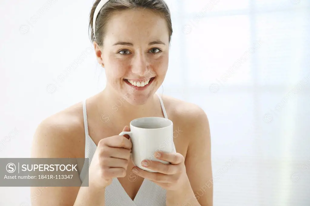 young woman holding a cup of tea in her hands and is smiling at the camera