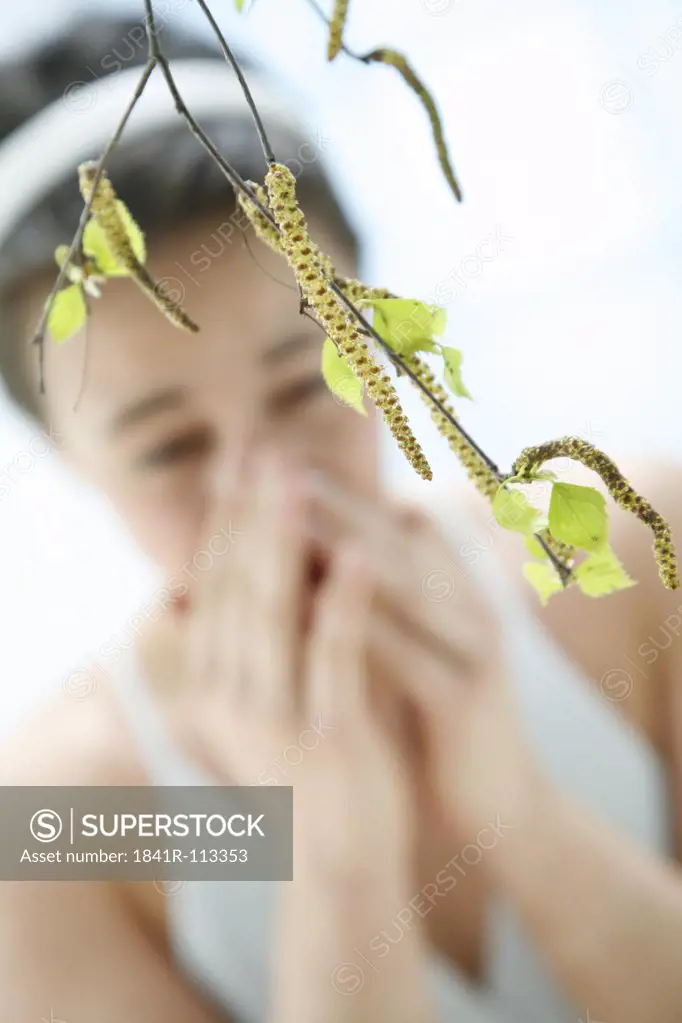 a branch with leaves of a birch tree - in the background blurred a young woman  sneezing