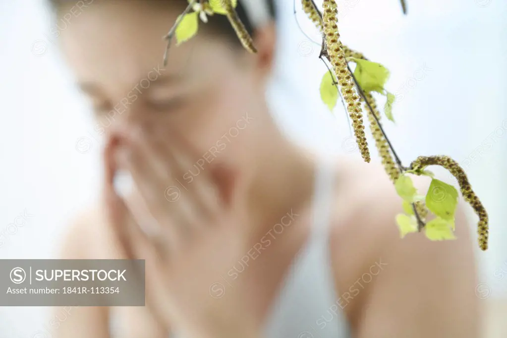a branch with leaves of a birch tree - in the background blurred a young woman  sneezing