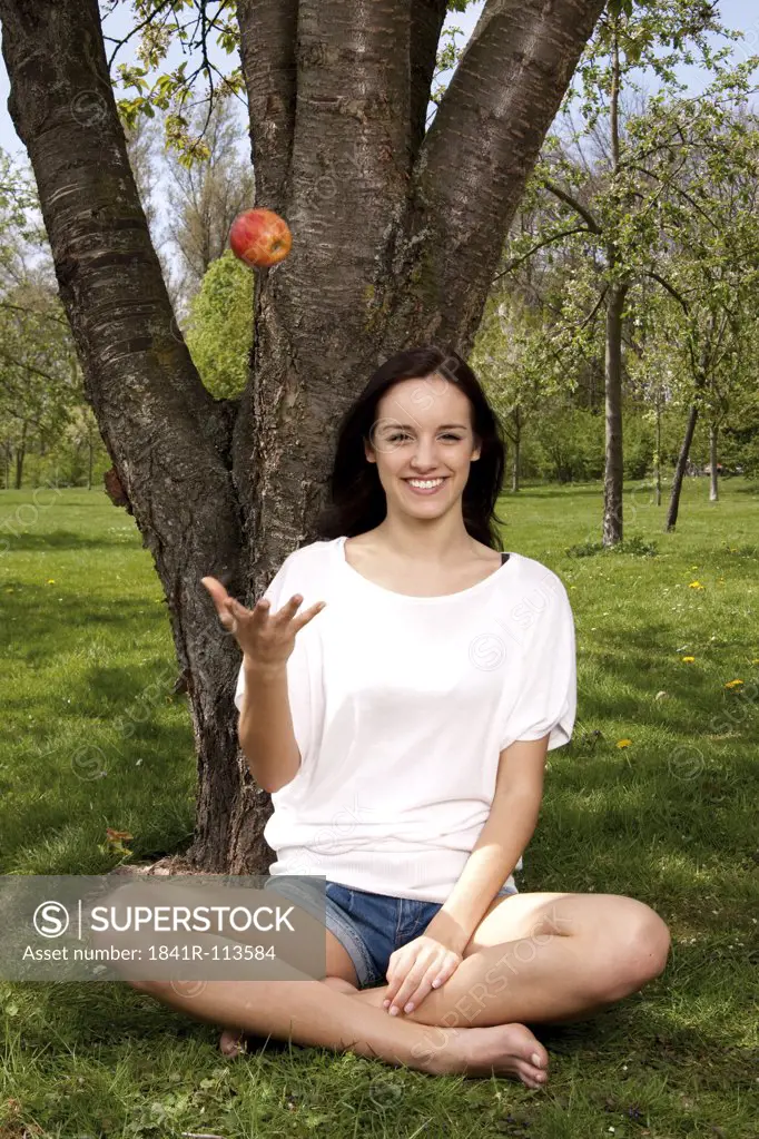 Young woman sitting with an apple on meadow