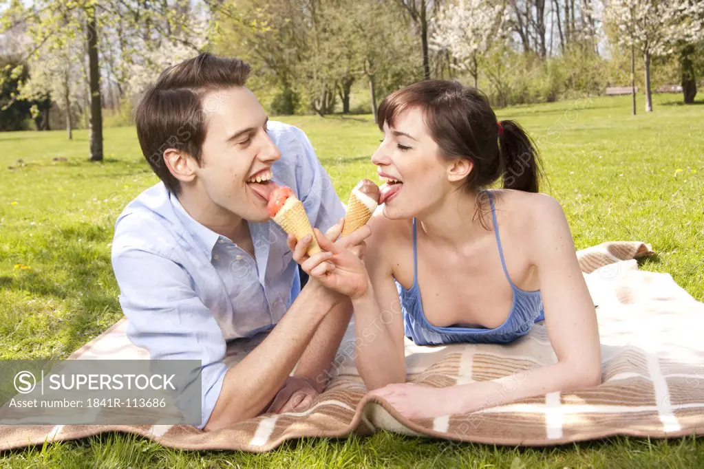 Young couple lying in meadow licking ice cones