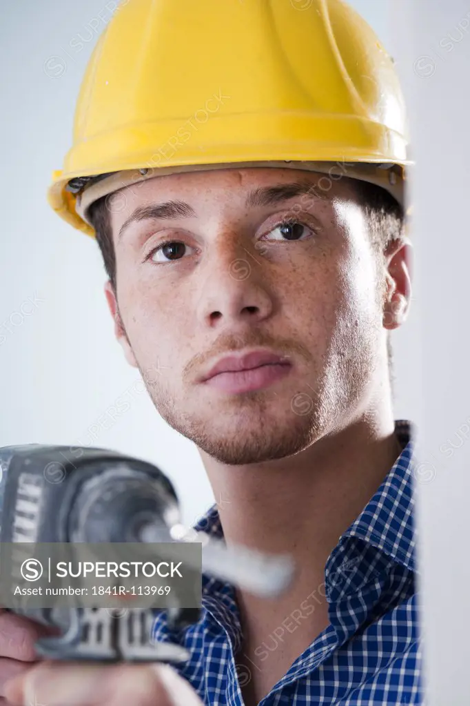 Young man wearing hard hat using drilling machine, portrait