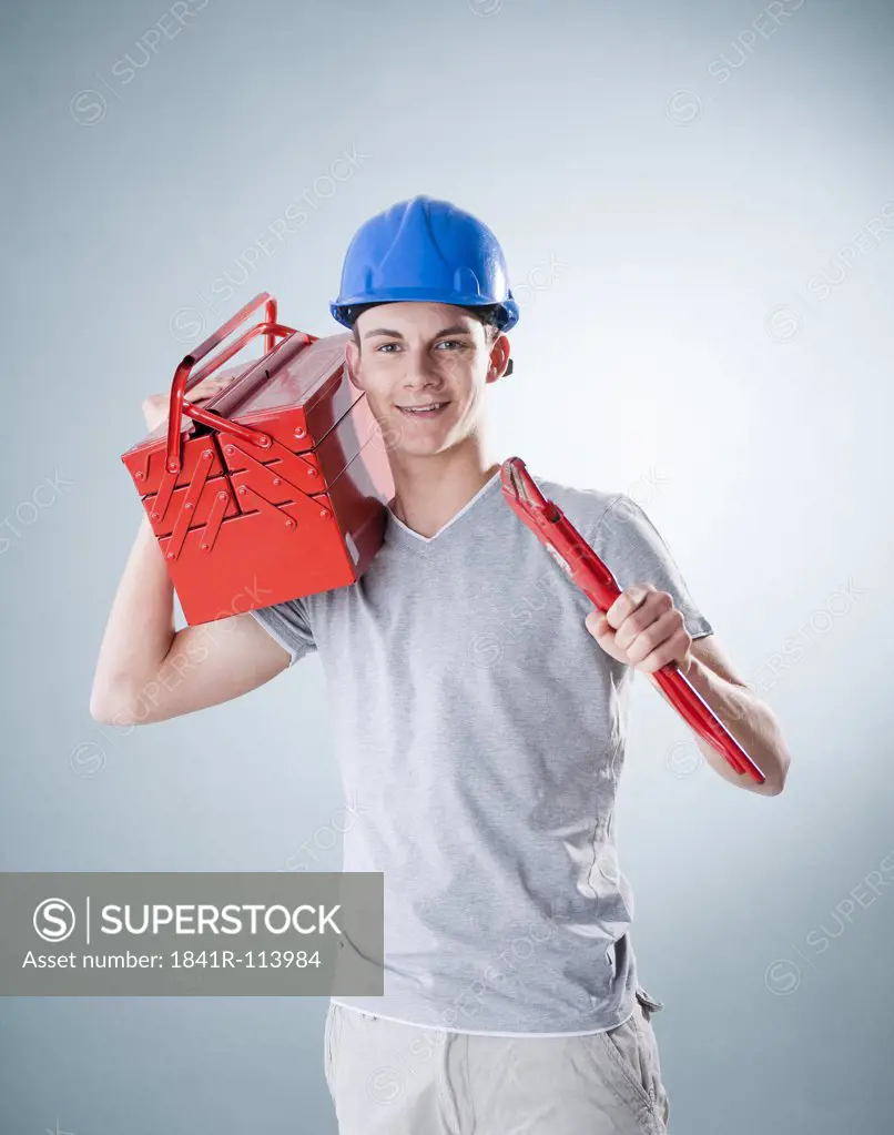 Young man wearing hard hat holding tools, portrait