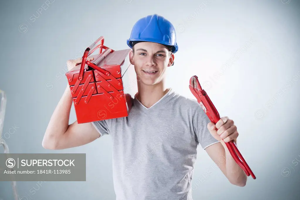 Young man wearing hard hat holding tools, portrait