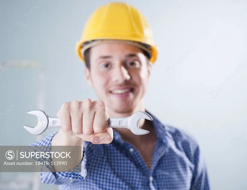 Young man wearing hard hat holding wrench, portrait