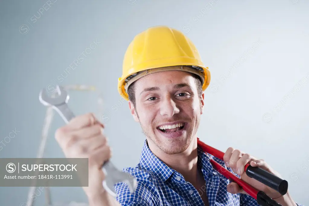 Young man wearing hard hat holding wrench, portrait