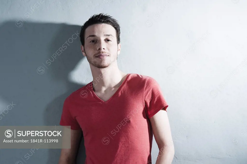 Young man wearing red T-shirt leaning against wall
