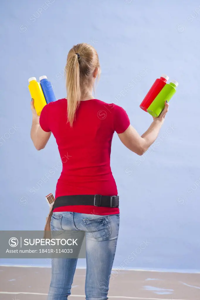 Young woman standing with different paint tins at a wall