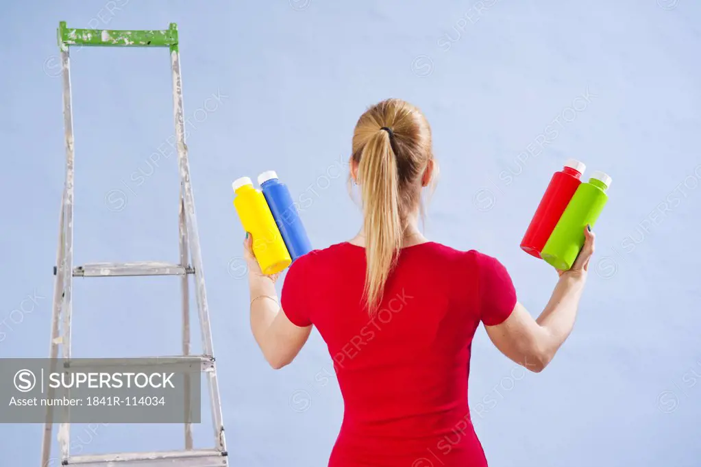 Young woman standing with different paint tins at a wall