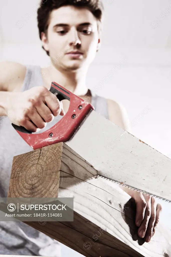 Young man sawing wooden block